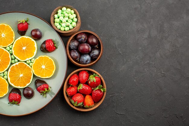 Top close-up weergave met chocolade bedekt fruit smakelijke met chocolade bedekte aardbei gehakte oranje groene snoepjes en kommen met verschillende bessen en snoep op donkere achtergrond