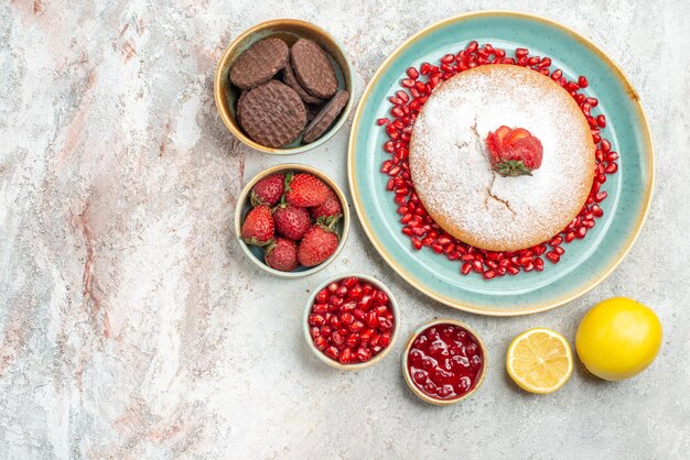 Top close-up weergave taarten met granaatappel plaat van cake van aardbeien en zaden van granaatappel citroen koekjes op tafel