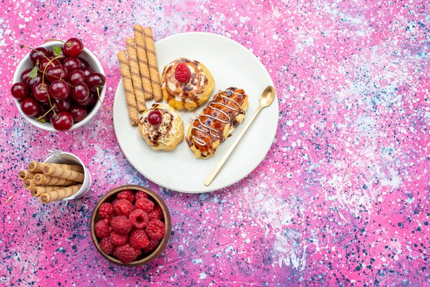 Top verre uitzicht heerlijke fruitige taarten met room en chocolade in witte plaat samen met vers fruit op de roze achtergrond cake zoete bak