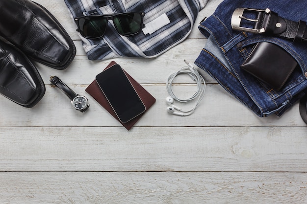 Top view accessoires om te reizen met man kleding concept. shirt, jean, mobiele telefoon op houten background.watch, zonnebril en schoenen op houten tafel.