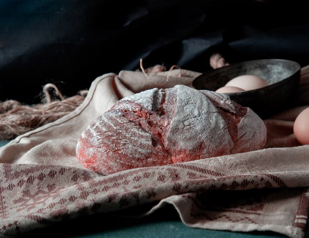 Traditioneel brood met witte bloem erop met eierkom rond op een rustieke handdoek.