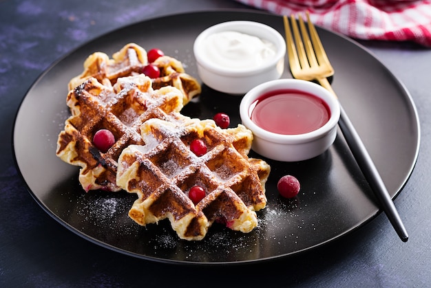 Traditionele Belgische wafels met bessen, zure room en jam op donkere tafel.