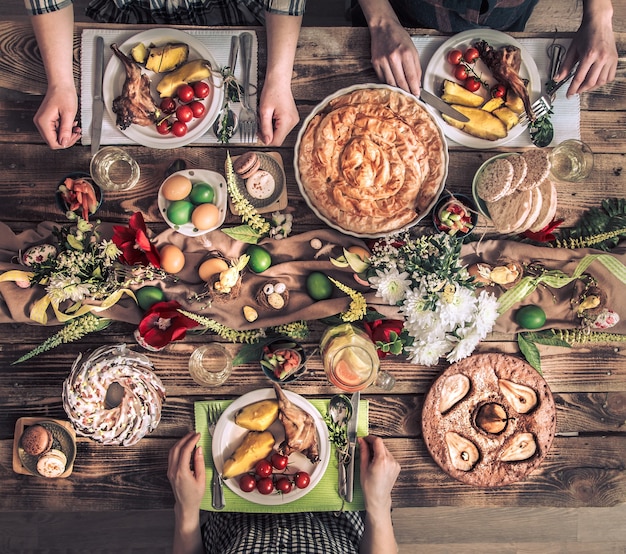 Traditionele paasviering, paasfeest. Vakantievrienden of familie aan de feesttafel met konijnenvlees, groenten, taarten, eieren, bovenaanzicht. Vrienden handen samen eten en drinken.