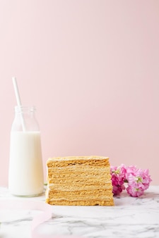 Traditionele russische cake medovik honingcake met fles melk en bloemen op roze achtergrond met ...
