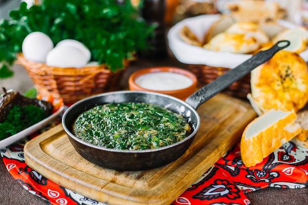 Gratis foto traditionele schotel kuku op het houten raadsei met greens brood zijaanzicht