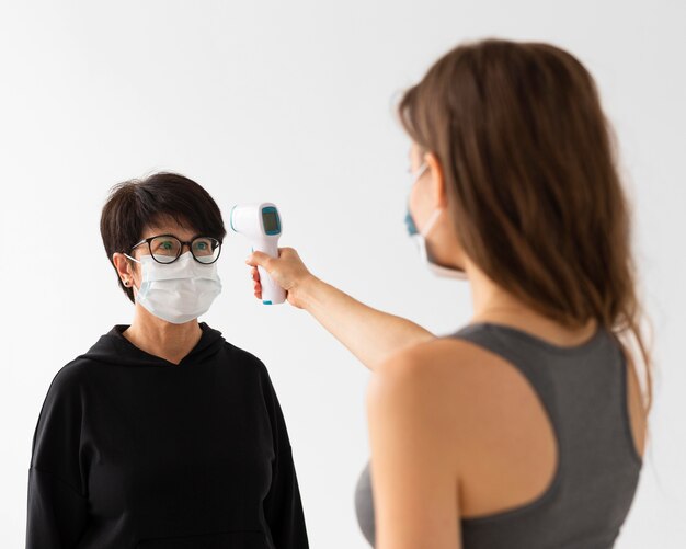 Trainer die de temperatuur van een vrouw scant terwijl hij medische maskers draagt