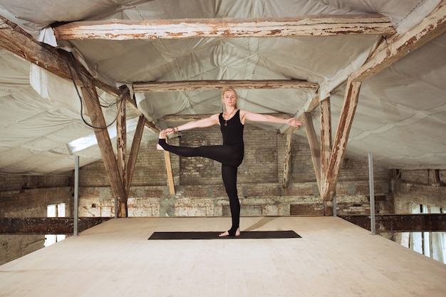 Trainer. Een jonge atletische vrouw oefent yoga op een verlaten bouwgebouw. Geestelijke en lichamelijke gezondheid. Concept van een gezonde levensstijl, sport, activiteit, gewichtsverlies, concentratie.