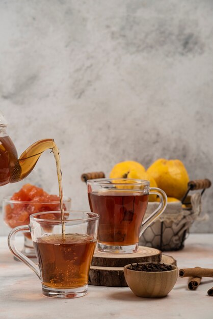 Transparante glazen theepot giet thee in glazen mok op marmeren tafel.