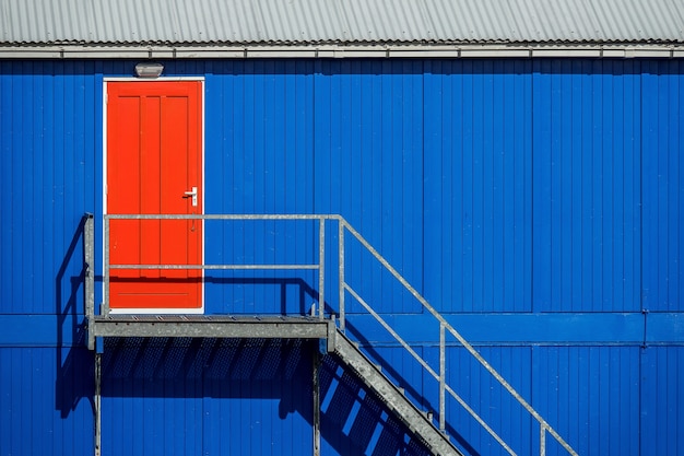 Trap bij de blauwe muur van een garage die naar de rode deur leidt