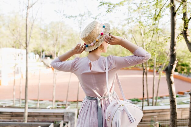 Trendy meisje met ouderwetse paarse jurk en strooien hoed genieten van prachtig uitzicht tijdens wandeling