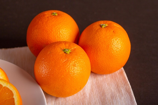 Tres naranjas frescas sobre la mesa, cerca de un plato de naranjas en rodajas, vista cerrada