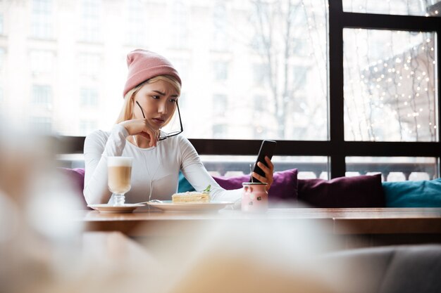 Triest fronsen jonge vrouw met behulp van mobiele telefoon in café