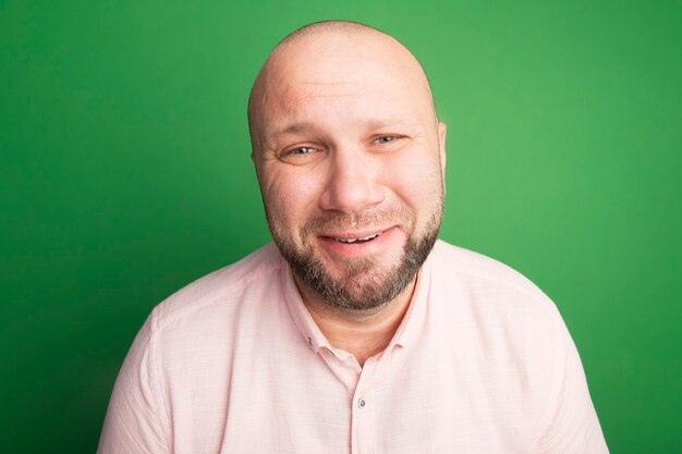 Gratis foto triest recht vooruit kijken kale man van middelbare leeftijd met roze t-shirt geïsoleerd op groen