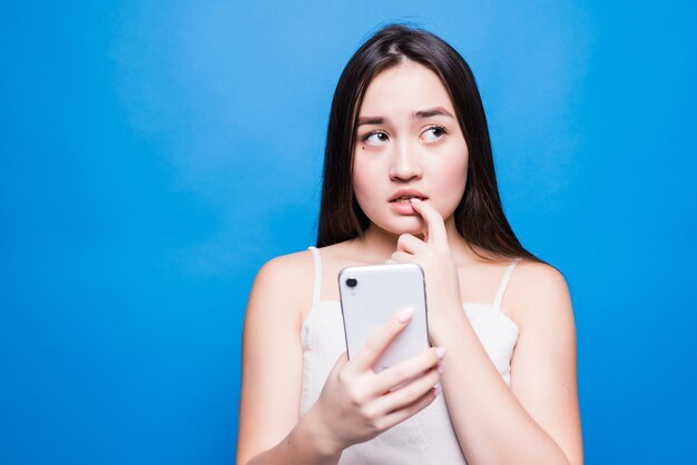 Triest sombere aziatische vrouw met behulp van smartphone geïsoleerd op een blauwe muur