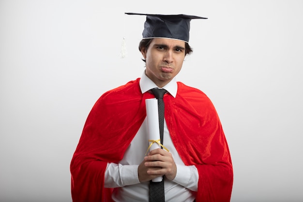 Trieste jonge superheld man kijken camera dragen stropdas en afgestudeerde hoed met diploma