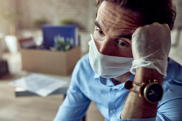 Gratis foto trieste zakenman die op kantoor zit en denkt na het verliezen van zijn baan als gevolg van een pandemie van het coronavirus