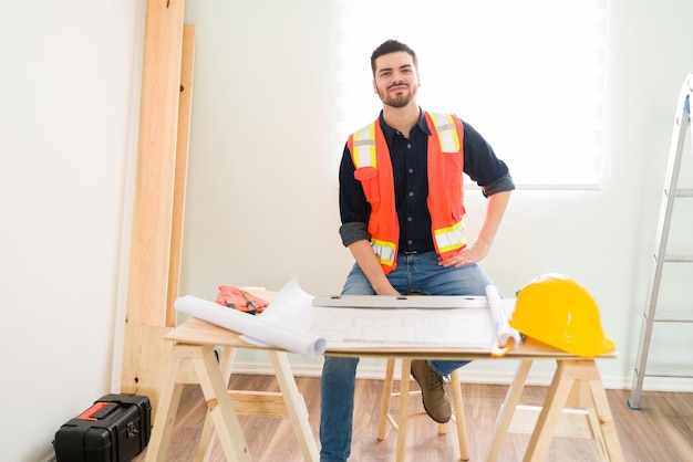 Trotse mannelijke aannemer geniet van een dag op het werk en controleert de blauwdrukken tijdens de bouw van een nieuw huis