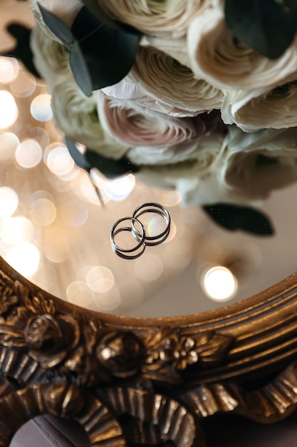 Trouwringen van de bruid en bruidegom op een spiegelend oppervlak met boke in de buurt van verse bloemen.