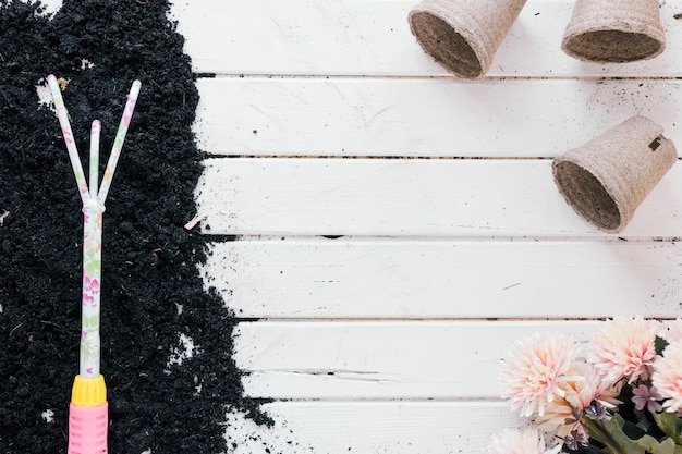 Gratis foto tuinieren hark op de bodem over houten tafel met turf pot en bloemen