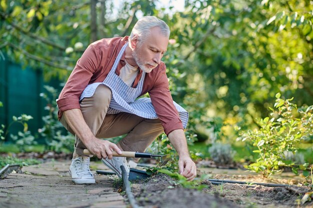 Tuinieren. Man van middelbare leeftijd aan het werk in een tuin met gtareden-inventaris