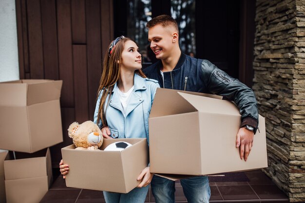 Twee aantrekkelijke personen met dozen op handen verhuizen naar een nieuw huis.