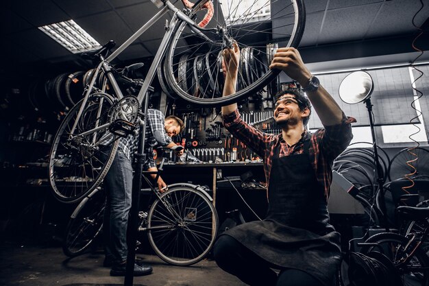 Twee aantrekkelijke reparateurs repareren een kapotte fiets in hun donkere werkplaats.