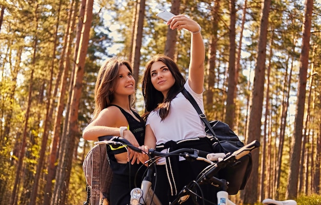 Twee aantrekkelijke sportieve vrouwtjes doen selfie na fietstocht in een herfstbos.