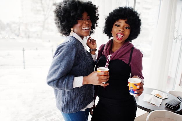 Twee Afro-Amerikaanse vrouwen met krullend haar dragen truien met kopjes thee in café binnen