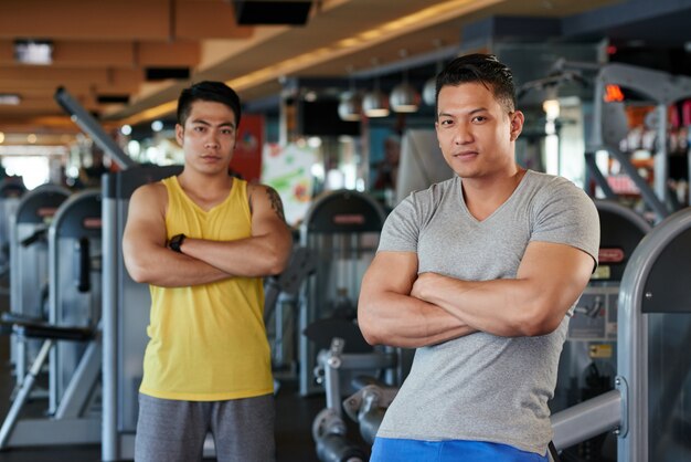 Twee atletische Aziatische mannen met gekruiste armen poseren in de sportschool