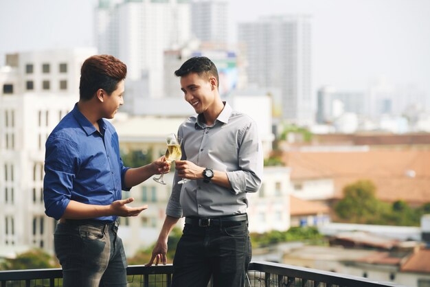 Twee Aziatische mannelijke vrienden die en van champagne babbelen genieten bij stedelijke partij op het dak