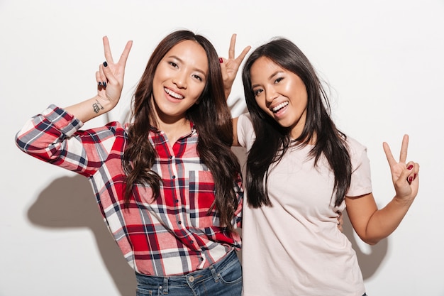 Twee Aziatische vrij vrolijke dameszusters die vredesgebaar tonen.