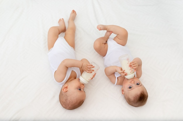 Twee baby's zuigen melk uit een fles die in een wiegje in de kinderkamer op een wit bed ligt