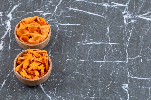 Twee bakjes stok- en driehoekchips op marmer.