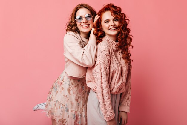 Twee beste vrienden die camera met glimlach bekijken. Studio shot van vrolijke glamoureuze meisjes geïsoleerd op roze achtergrond.