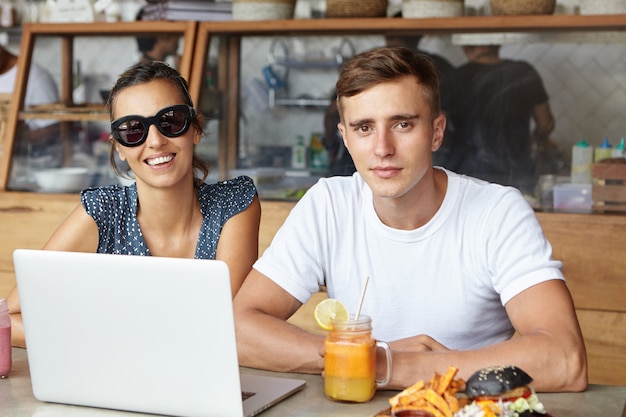 Twee beste vrienden met behulp van laptopcomputer tijdens de lunch, zittend in gezellig café interieur en kijken met een blij glimlach. Studenten studeren online op notebook pc