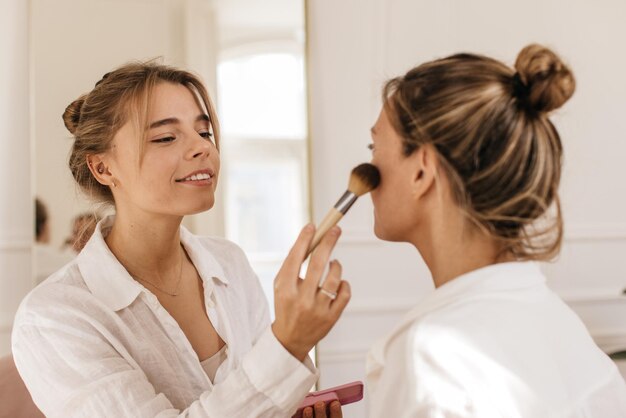 Twee blanke vrouwelijke modellen ondergaan cosmetische ingrepen, brengen blush aan terwijl ze een goed verzorgde huid hebben. Rituelen van vrouwelijke schoonheid, concept