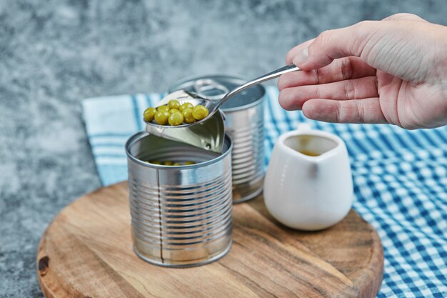 Twee blikjes gekookte groene erwten, een tafelkleed en een hand met een lepel.