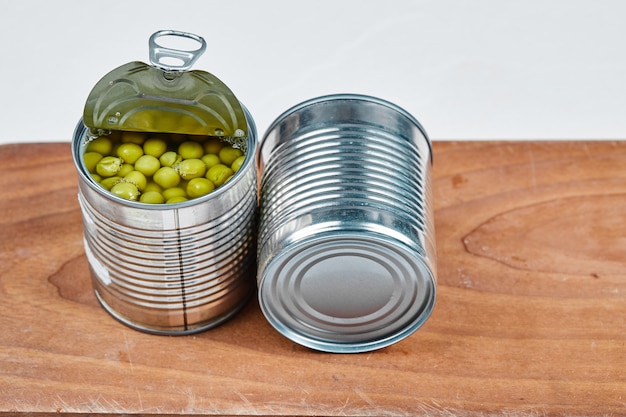 Twee blikjes gekookte groene erwten op een houten bord.