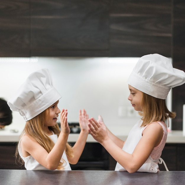 Gratis foto twee broers en zussen in chef-kok hoed en schort spelen keuken