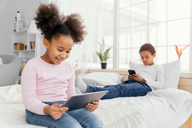 Twee broers en zussen thuis samen spelen op tablet en smartphone