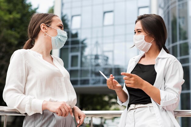 Twee collega's die tijdens pandemie buiten chatten terwijl ze maskers dragen