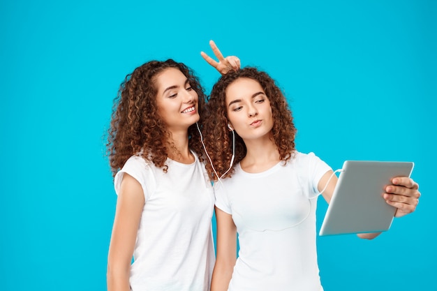 Twee dames tweeling maken selfie op tablet over blauw.