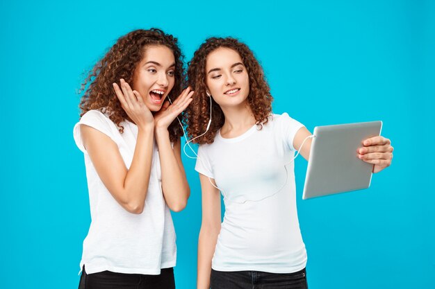 Twee dames tweeling maken selfie op tablet over blauw.