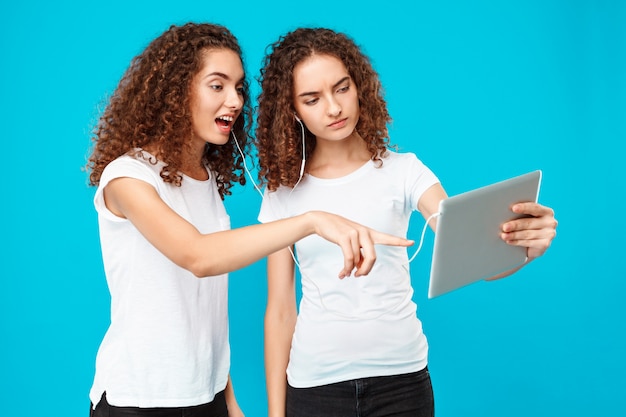 Twee dames tweelingen kijken naar tablet, verrast over blauw.