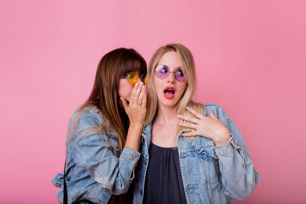 Twee emotionele vrouwen roddelen omhoog op roze muur