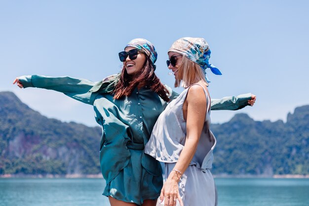 Twee gelukkige de toeristenvrienden van de vrouwenblogger in zijden kostuum en sjaal en zonnebril op vakantiereis rond thailand op Aziatische boot, nationaal park Khao Sok.