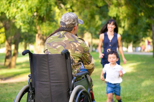 Twee gelukkige kinderen en hun moeder rennen naar gehandicapte gepensioneerde militaire vader en knuffelen hem. Veteraan van oorlog of naar huis terugkeren concept