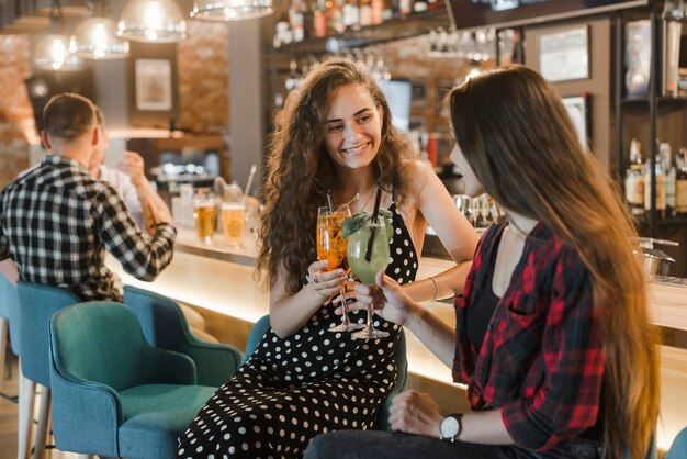 Twee gelukkige vrouwelijke vrienden die glas cocktail roosteren