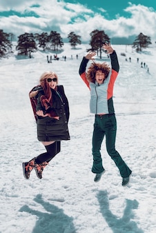 Twee gelukkige vrouwen die in de lucht springen en plezier hebben in de sneeuw