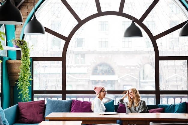Gratis foto twee gelukkige vrouwen zitten en praten in café